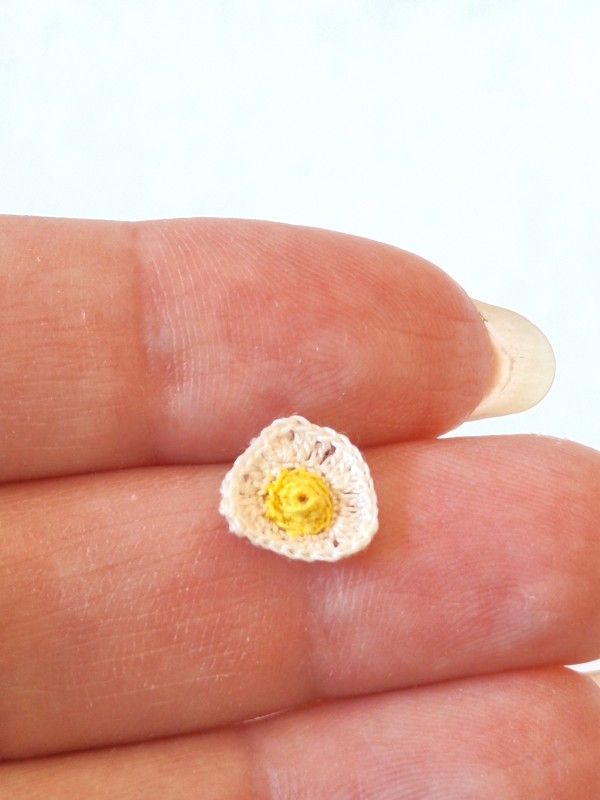Tiny micro crochet fried egg shown in hand to demonstrate miniature size