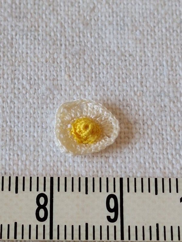 Tiny micro crochet fried egg shown in hand to demonstrate miniature size