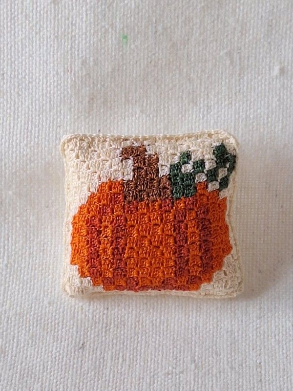 Orange and green C2C crochet pumpkin cushion displayed on a miniature shelf