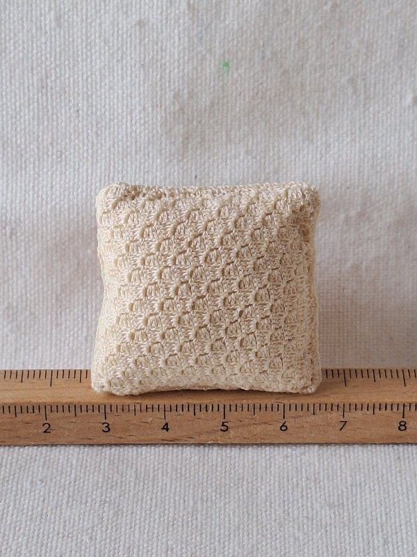Back of a handmade miniature crochet cushion showing the cream-coloured reverse side