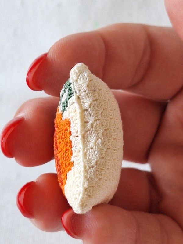 Side view of a tiny C2C crochet pumpkin cushion showing its three-dimensional shape