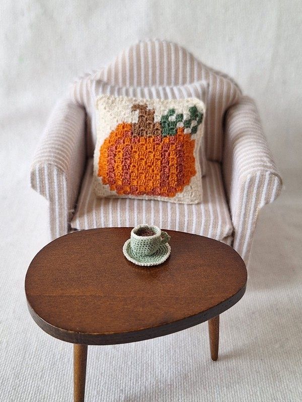 C2C crochet pumpkin cushion styled on a miniature armchair in a cosy autumn scene